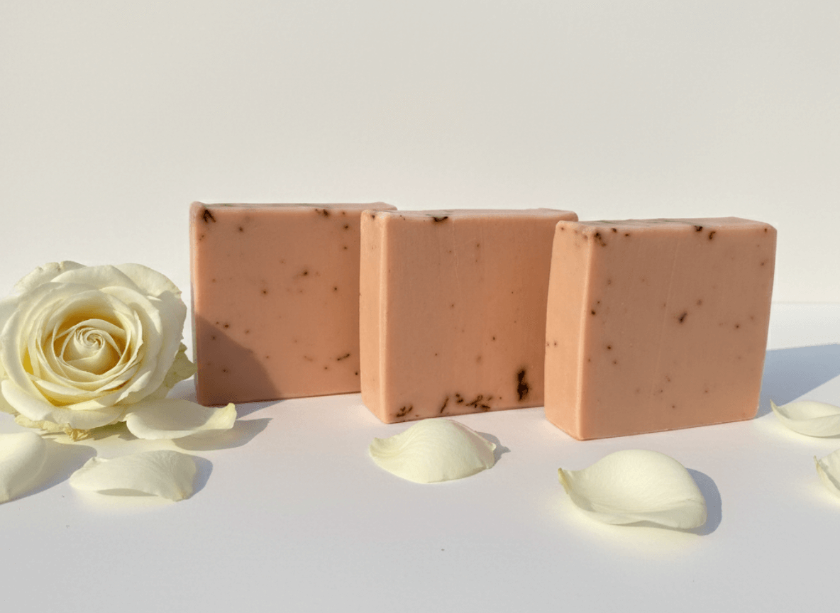 Three rectangular soap bars with visible textures on a white surface with a white rose and petals.