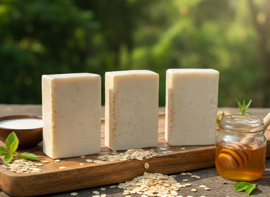 Three bars of soap on a wooden board with seeds and a jar of honey, set against a natural background.