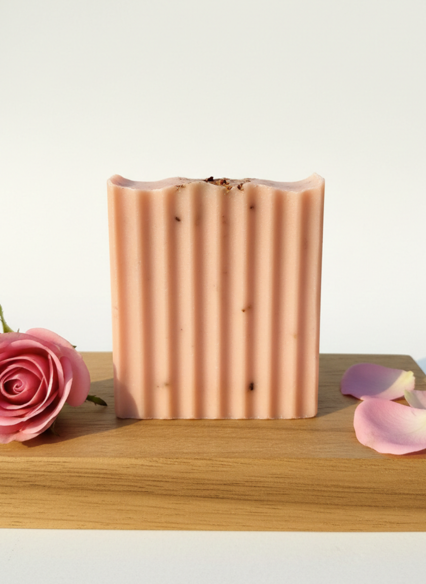 Bar of soap with a rose and petal on a wooden surface