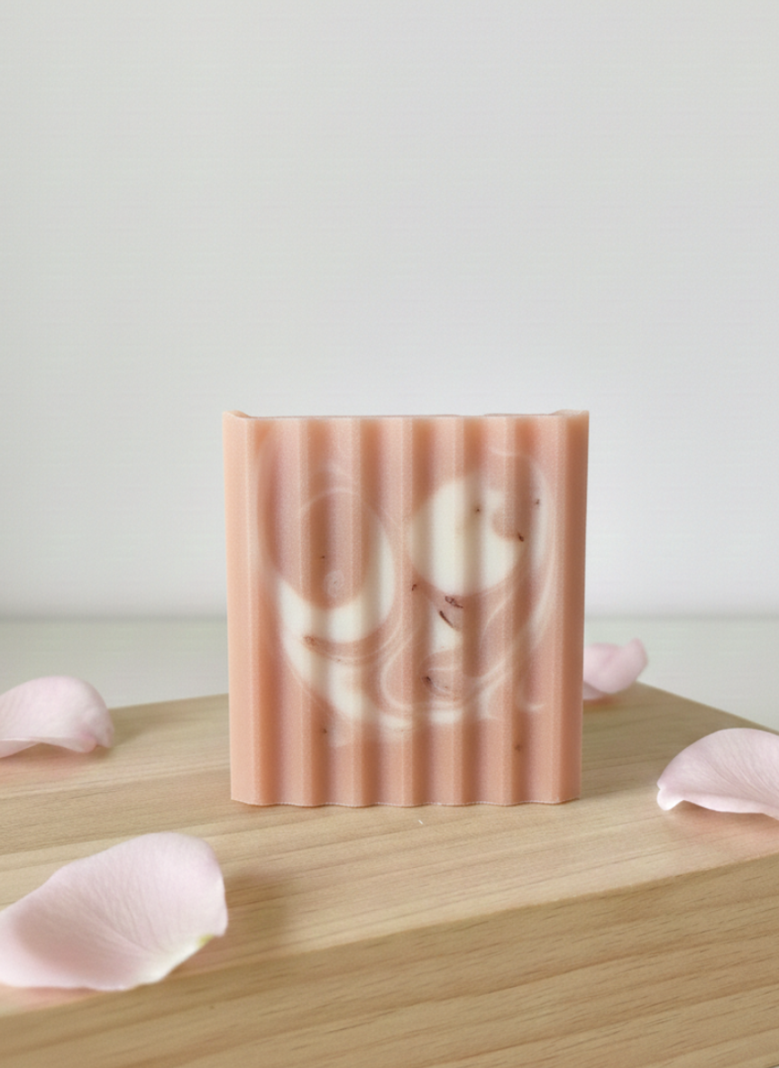 Bar of soap with floral design on a wooden surface with pink petals
