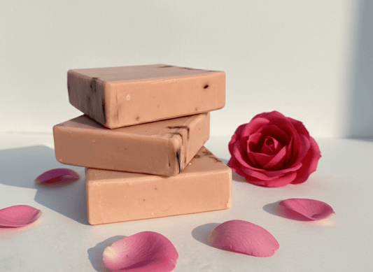 Three bars of soap stacked with a pink rose and petals on a light background